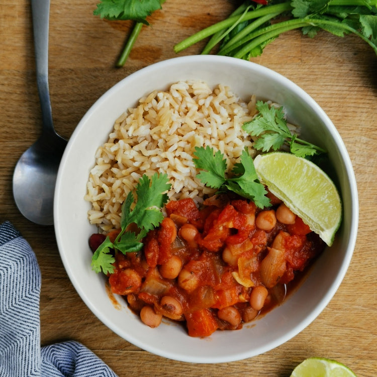 A white bowl with Channa Masala & Brown Rice, beans and limes from Fierce Fuel available for delivery in Squamish.