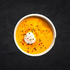 A ready-made bowl of Curried Parsnip Soup with sour cream on a dark background from Fierce Fuel in Squamish.