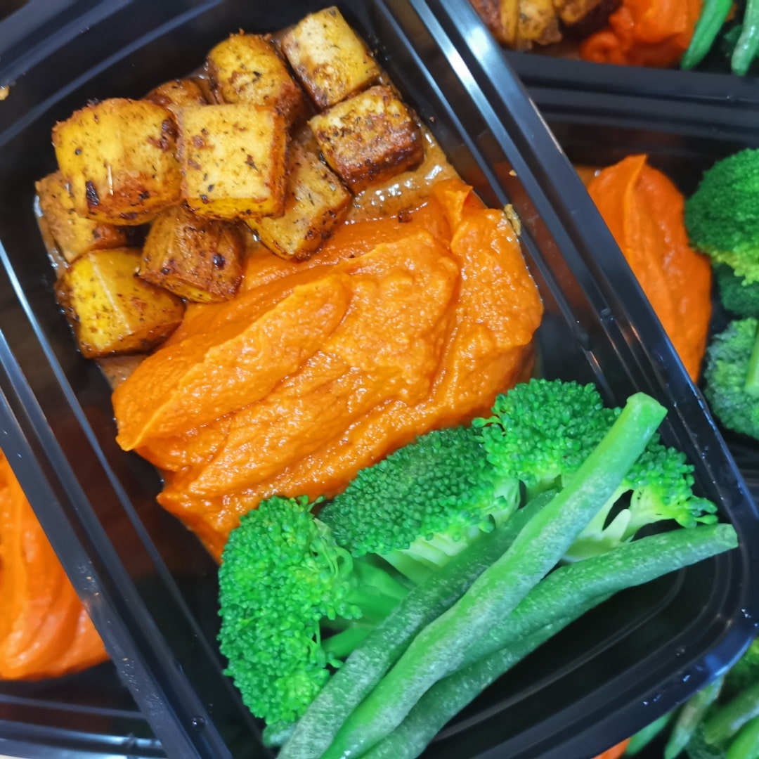 A healthy prepped meal delivery featuring a black plastic container with Cajun Tofu from Fierce Fuel.